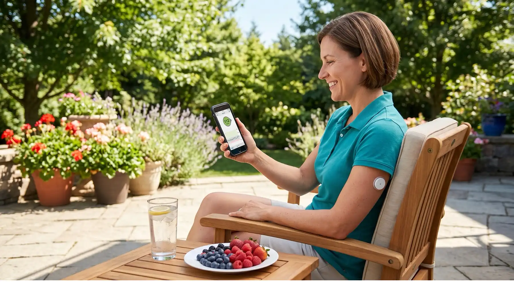 Woman in a garden chair checks a smartphone health app, wearing a wireless arm sensor; a plate of berries and a glass of water sit on the table nearby.